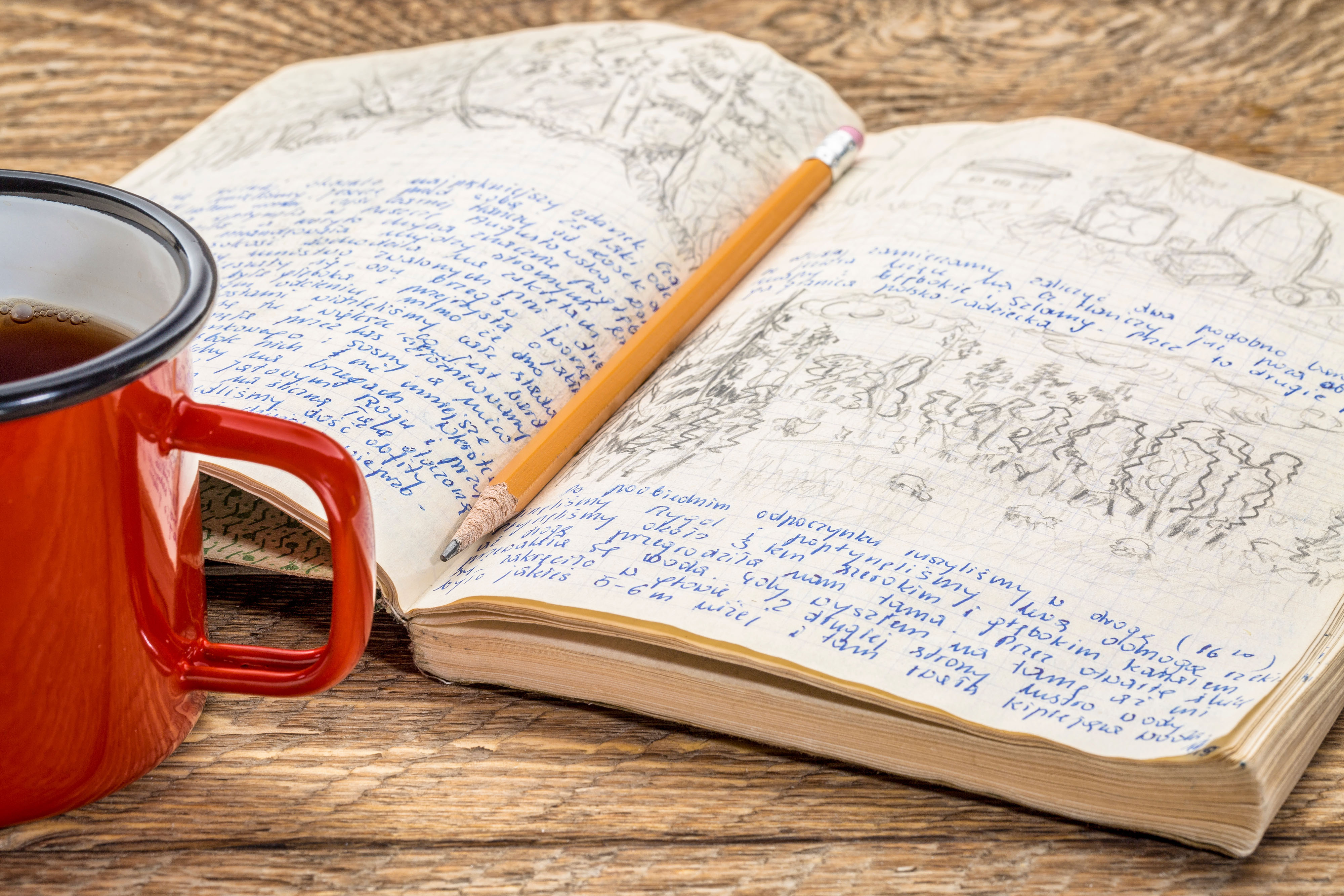 Close-up of handwritten goals journal with a warm cup of tea beside it on a wooden desk