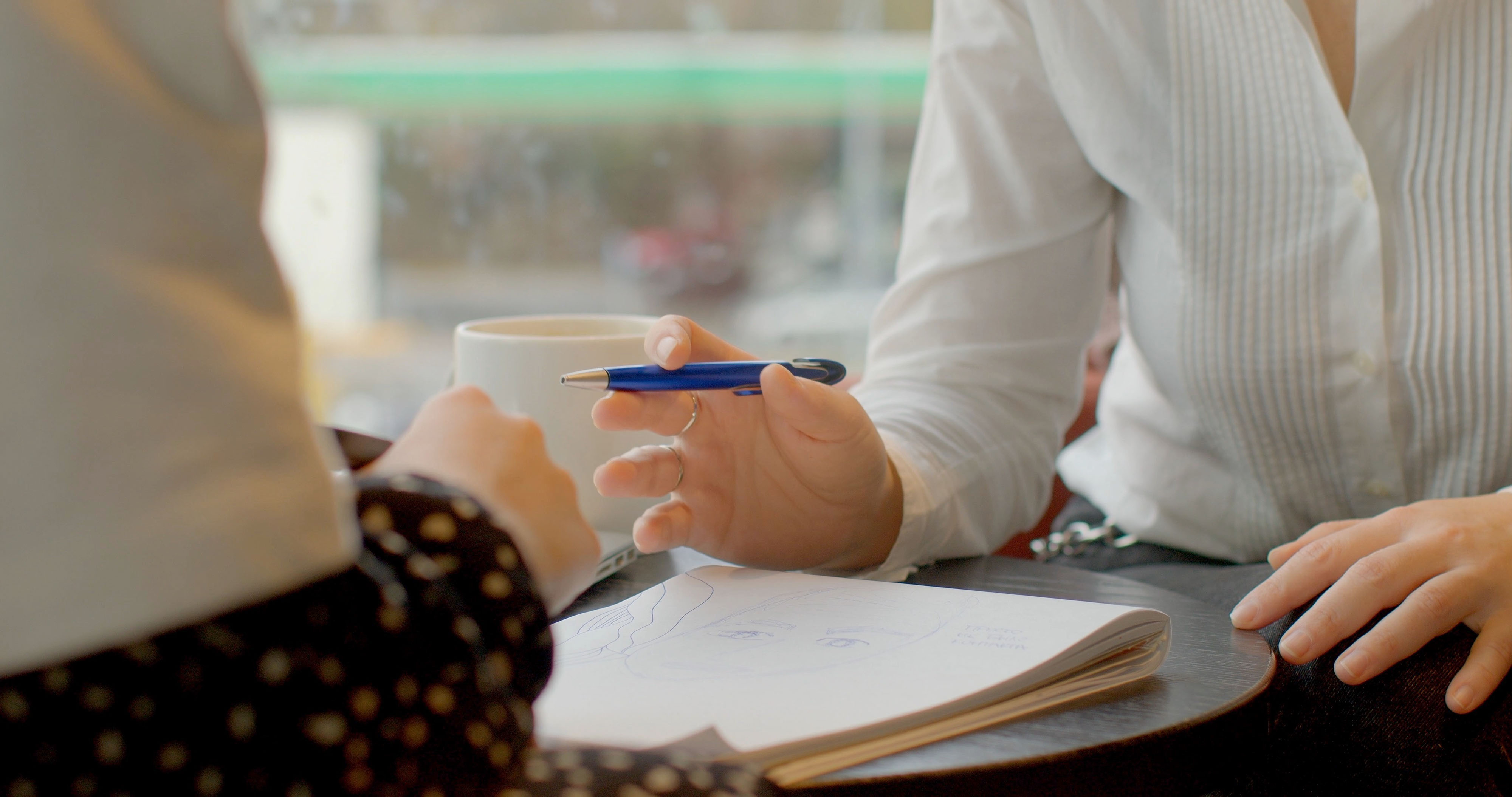 Two people collaborating over a shared document at a bright cafe table with natural light