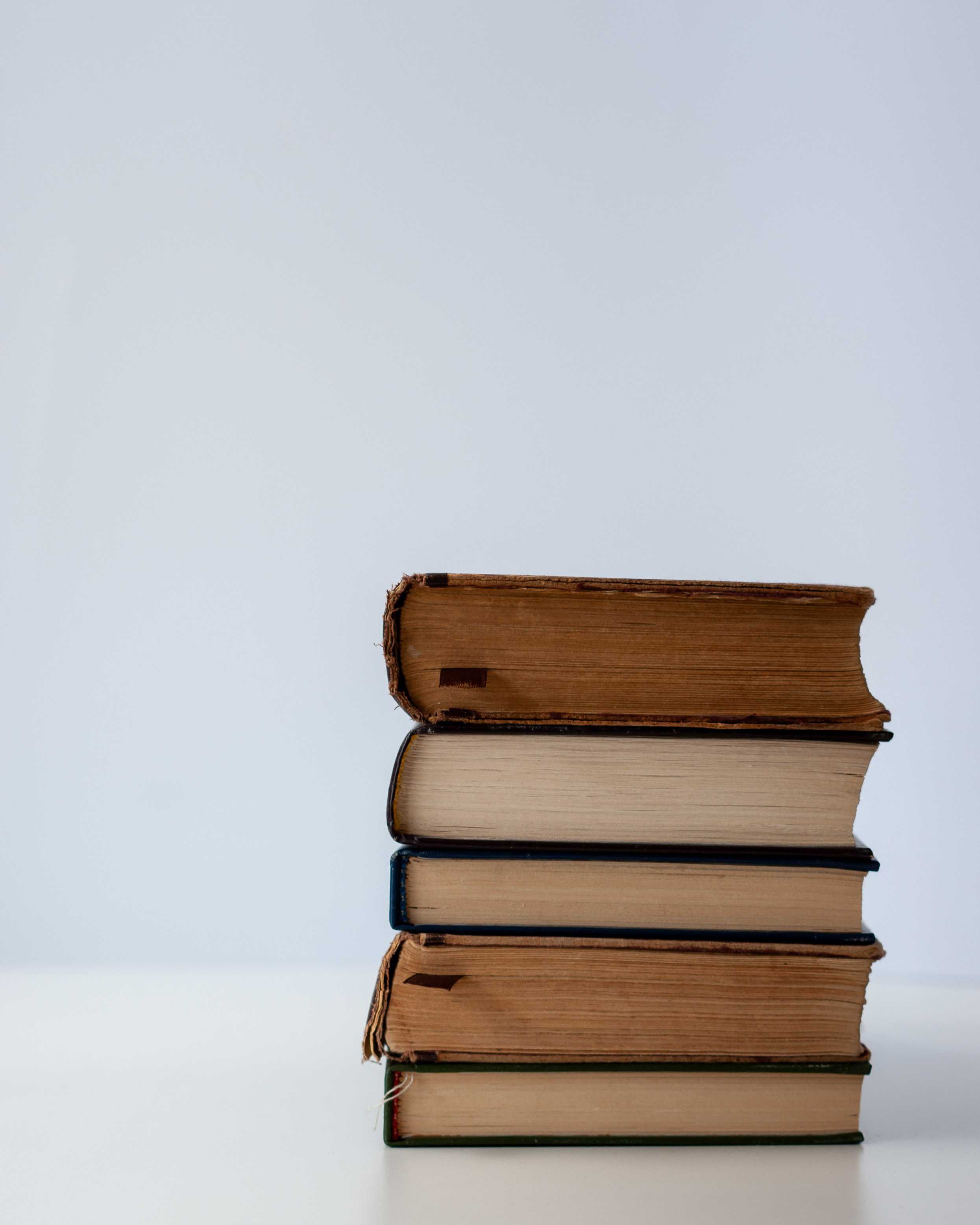 Stack of three well-worn paperback books with soft natural light casting gentle shadows on a white surface